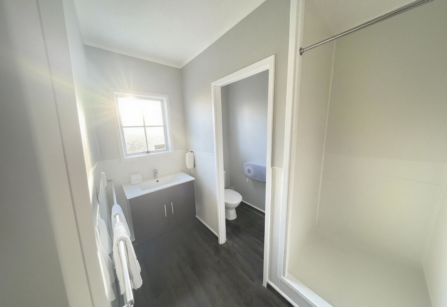A bathroom with a window, a sink, a toilet, and a shower area.