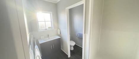 A bathroom with a window, a sink, a toilet, and a shower area.