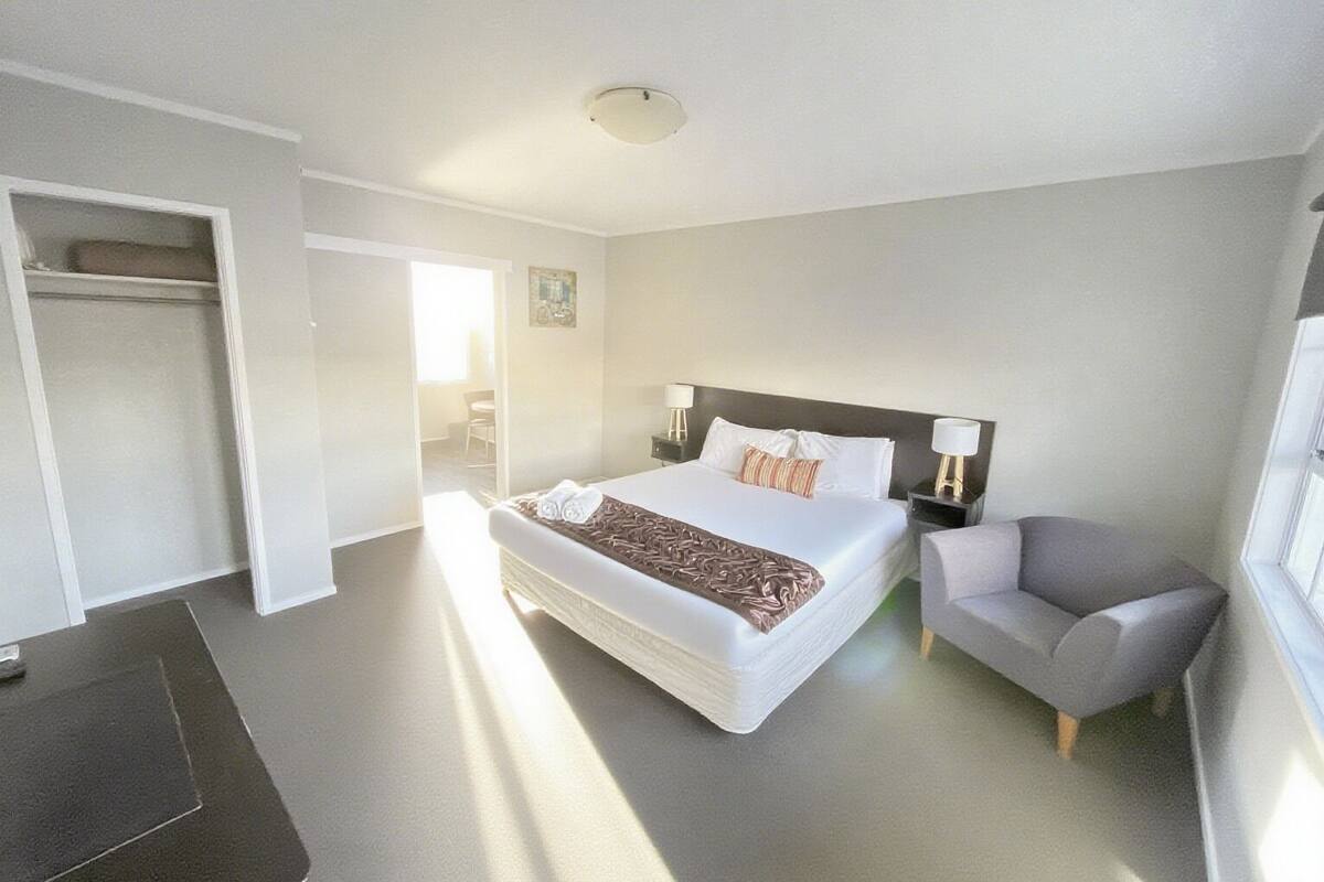 A modern hotel room with a large bed, bedside tables, a chair, and a walk-in closet.