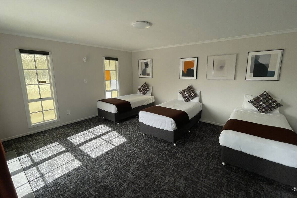 A hotel room with three beds, large windows, and artwork on the walls.