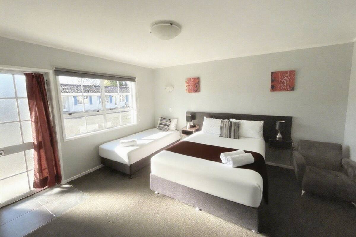 A hotel room with a bed, a chair, a desk, and a window.