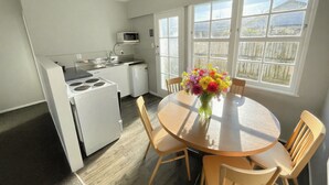 A compact kitchen with a stove, microwave, and refrigerator, a dining table with chairs, and a window with a view of a mountainous landscape. - Boundary Court Motor Inn (Hamilton)