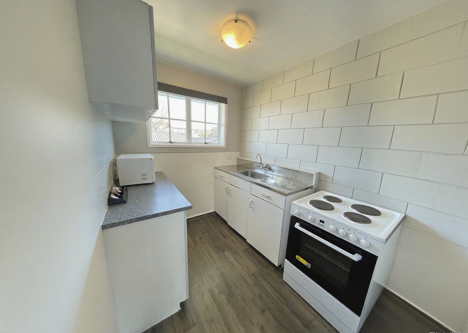A compact kitchen with white cabinets, a countertop, a sink, and a stove.
