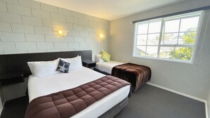 A hotel room with a large bed, a smaller bed, a window with a view, and a brick-patterned wall. - Boundary Court Motor Inn (Hamilton)