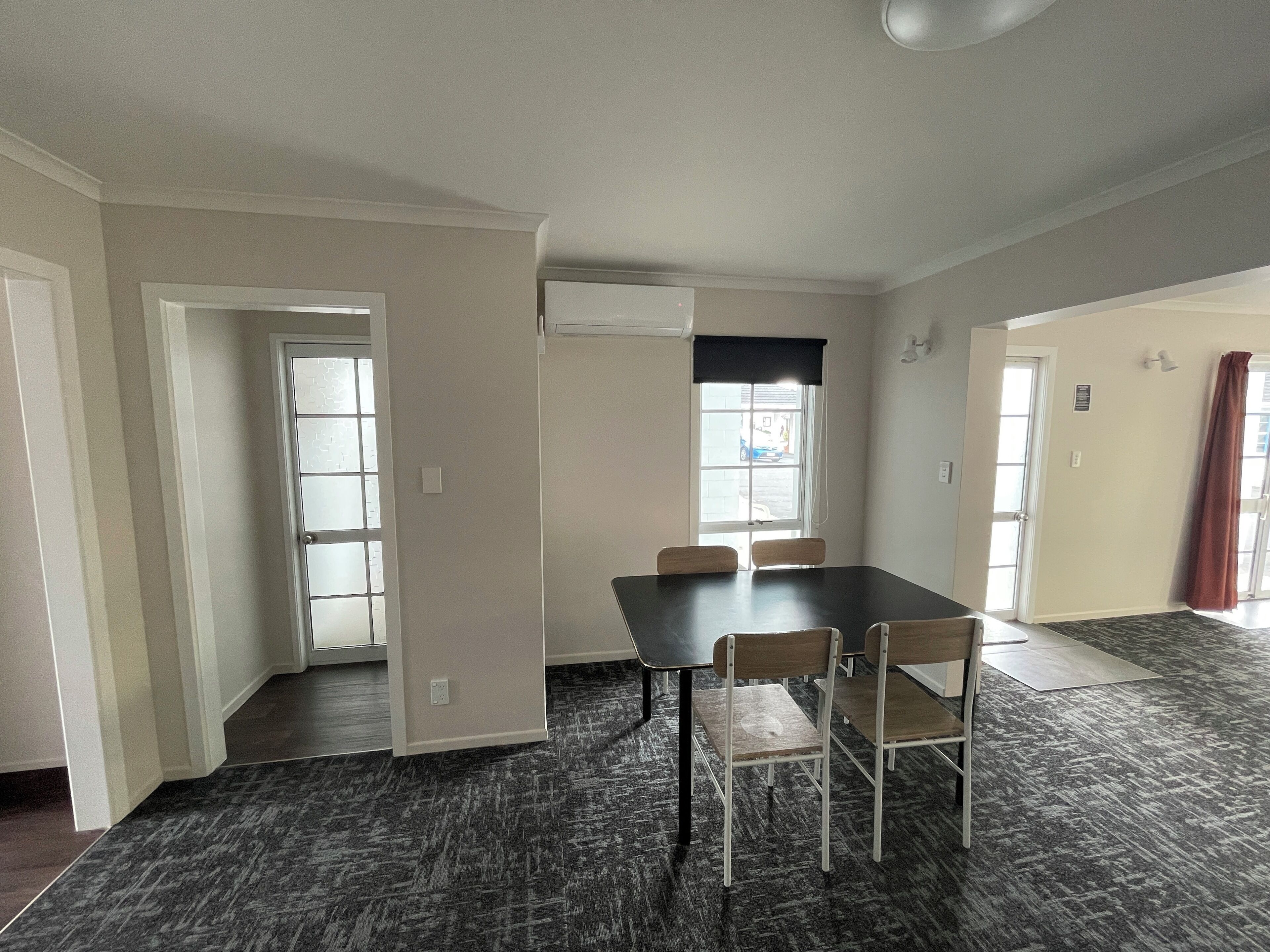 Une pièce spacieuse comprenant une grande table à manger et quatre chaises, une fenêtre avec des stores et une porte donnant sur une autre pièce.