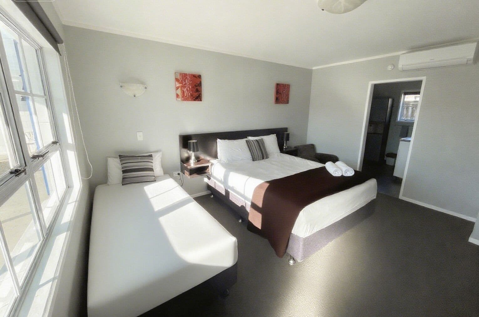 A hotel room with a bed, bedside table, lamp, and a bench.