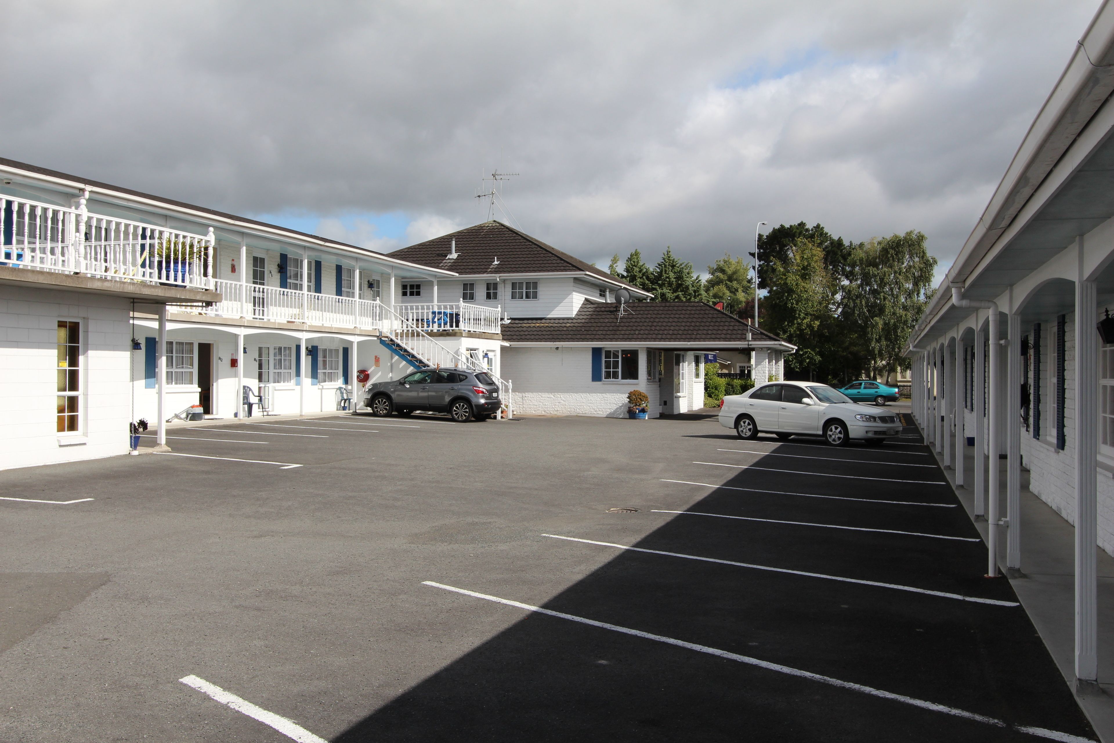 A motel with a central building and two wings, featuring a parking lot with several cars.