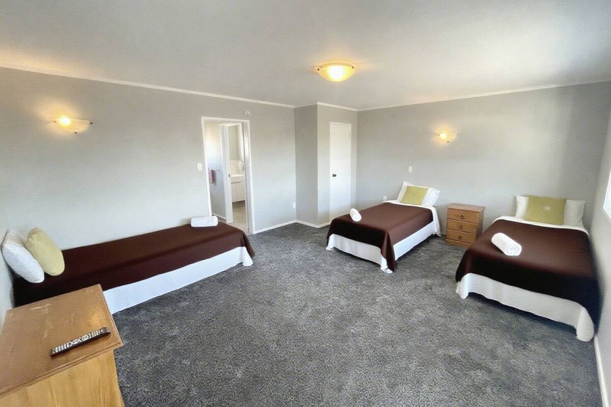A room with three single beds, a wooden dresser, and a small desk with a chair.