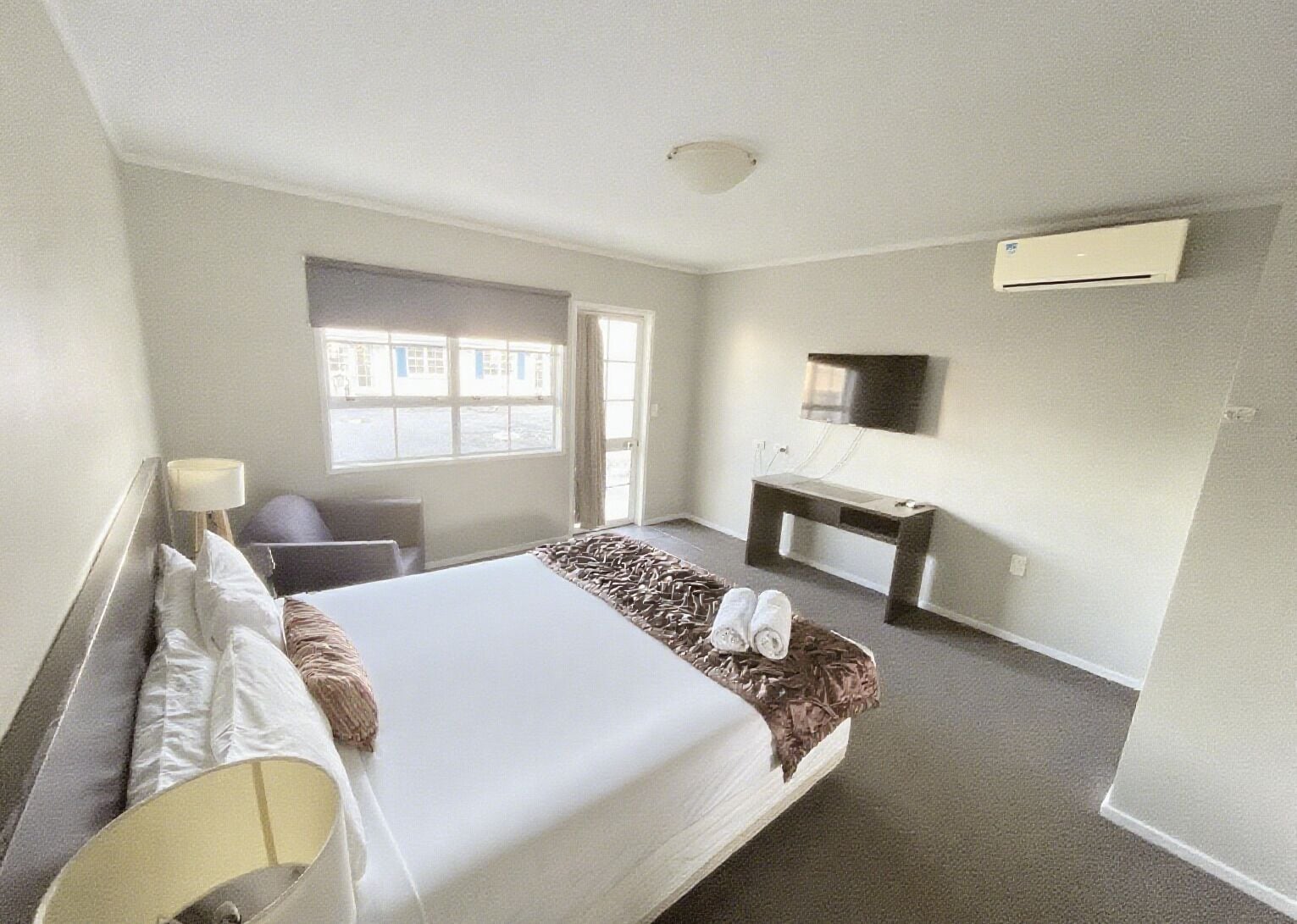 A hotel room with a bed, a desk, a chair, a TV, and a window.