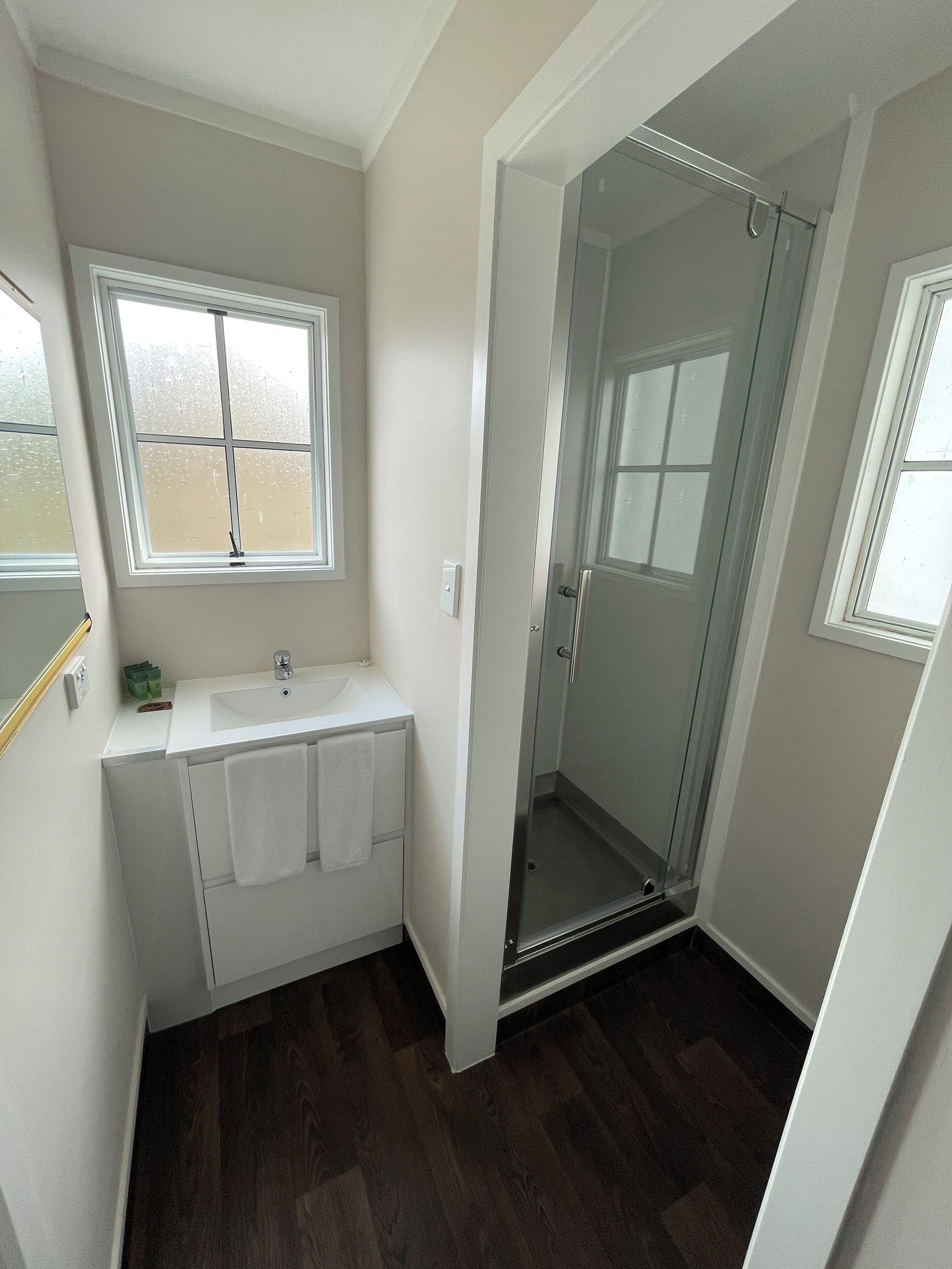 Un baño con lavamanos blanco, cabina de ducha de cristal y ventana.
