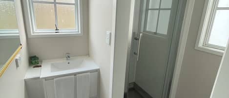 Un baño con lavamanos blanco, cabina de ducha de cristal y ventana.
