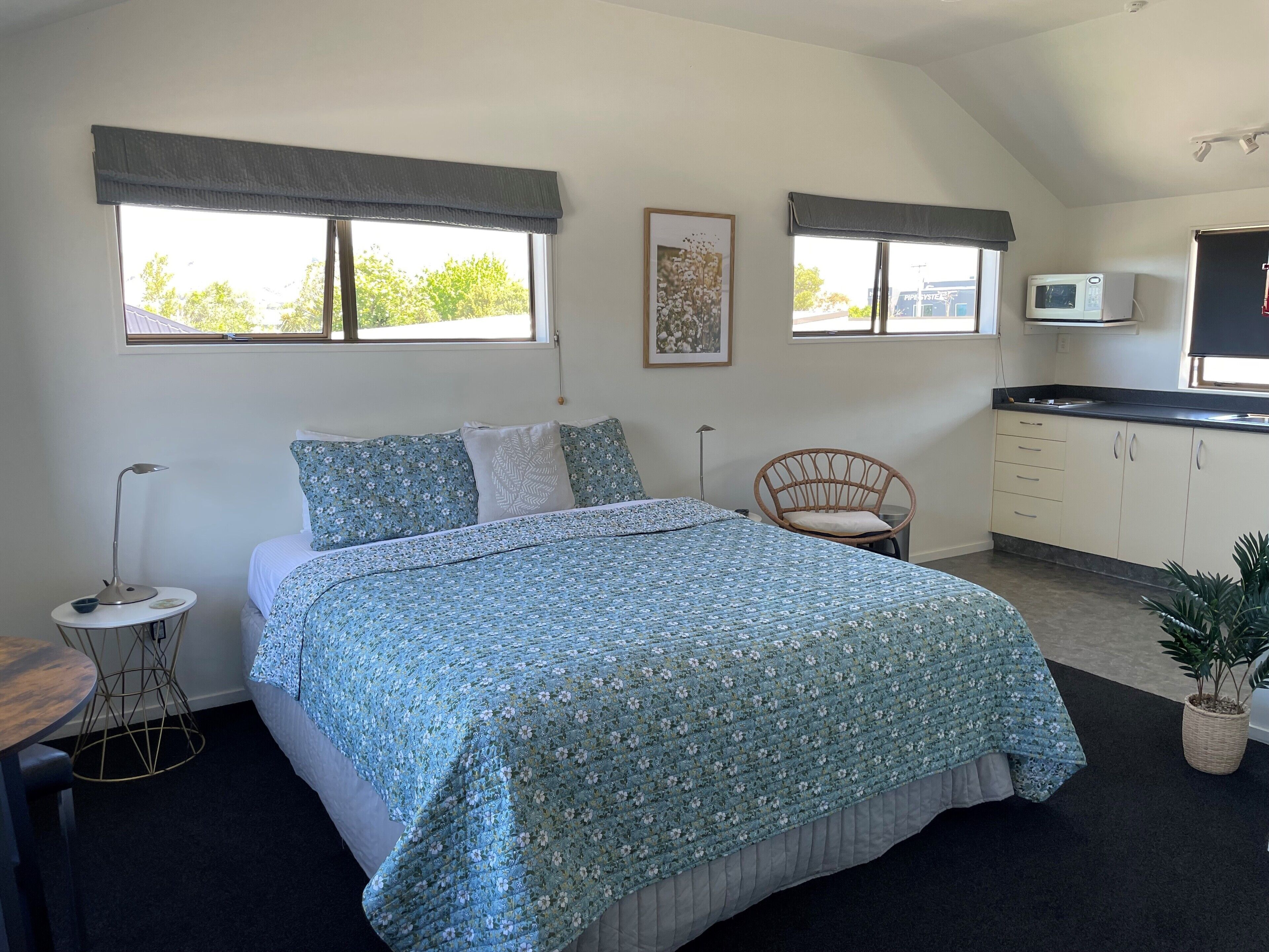 A bedroom with a bed, a chair, a small table, and a kitchenette.