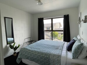 A bedroom with a bed, a window with curtains, a potted plant, and a mirror on the wall. - Colonial Motel (Blenheim)