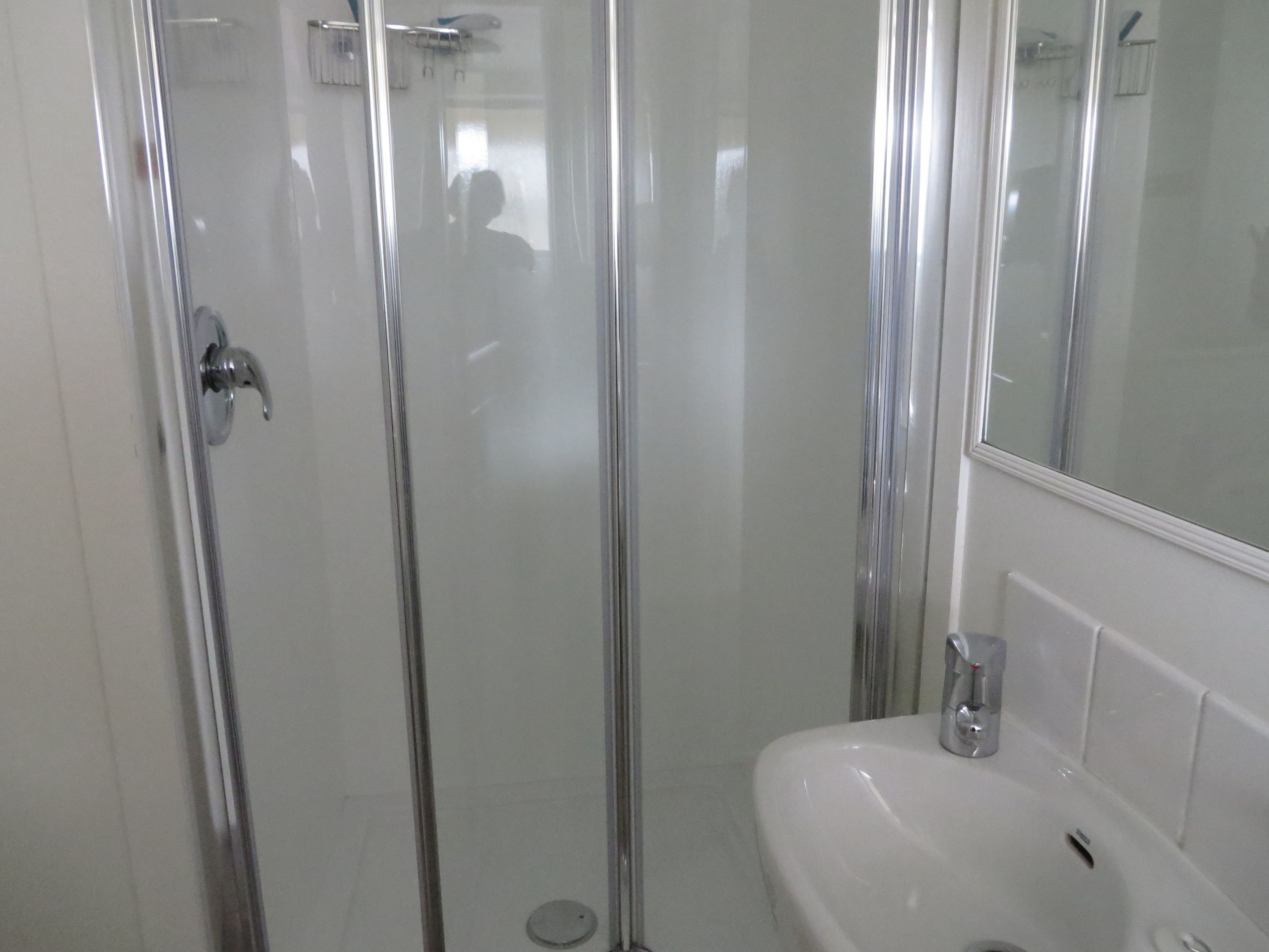 Una dutxosa amb envidriat, un lavabo blanc i un mirall.