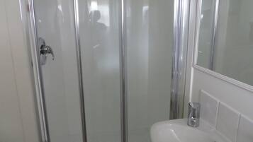 Una dutxosa amb envidriat, un lavabo blanc i un mirall.