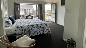 A bedroom with a bed, a chair, a balcony with a table and chairs, and a view of a building outside.
