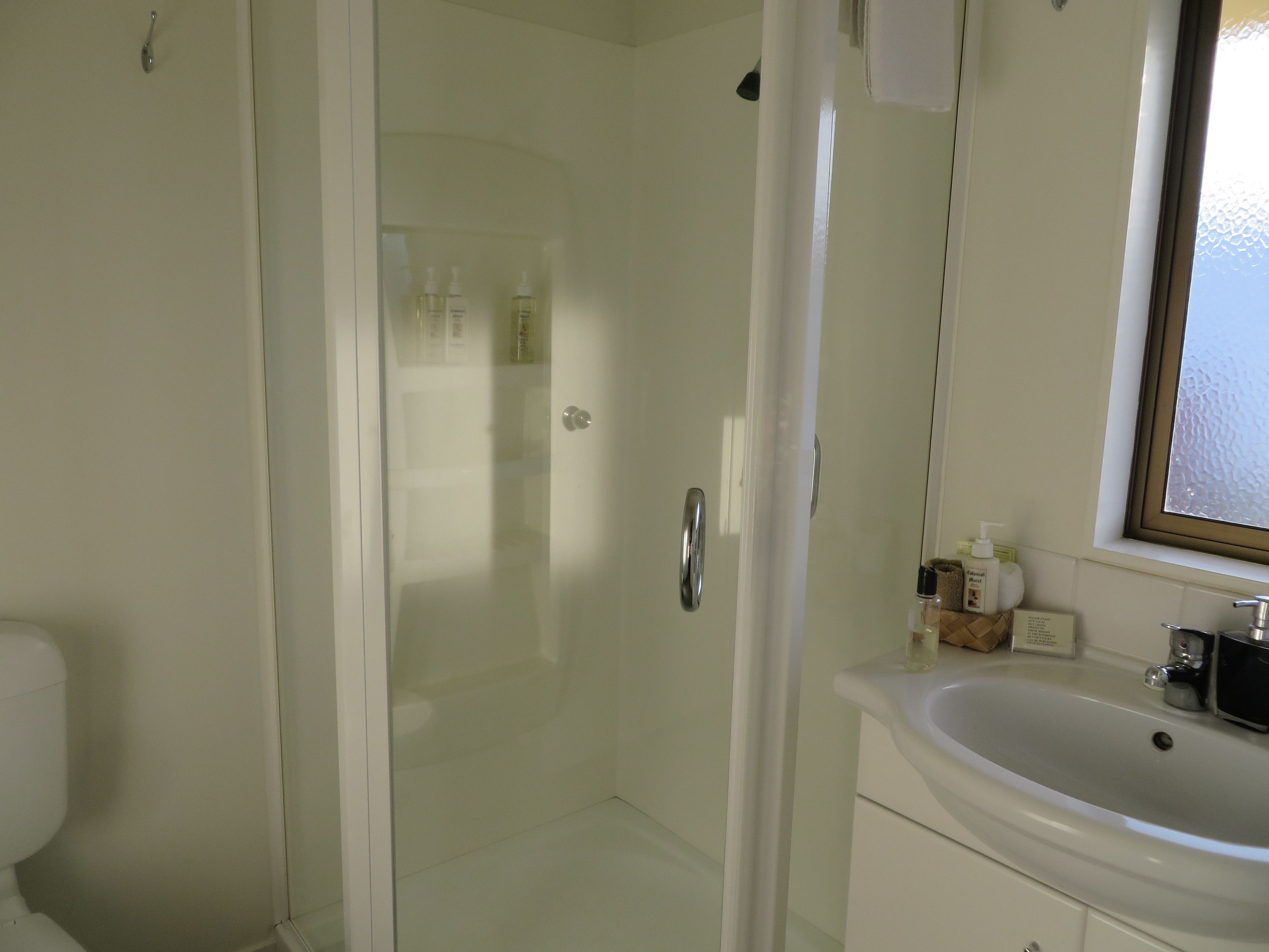 Un baño con ducha acristalada, lavabo blanco y artículos de tocador sobre el mostrador.