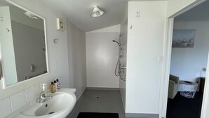 A bathroom with a sink, mirror, shower, and a small rug on the floor.