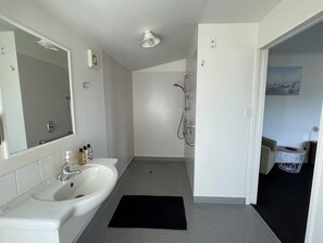 A bathroom with a sink, mirror, shower, and a small rug on the floor. - Colonial Motel (Blenheim)