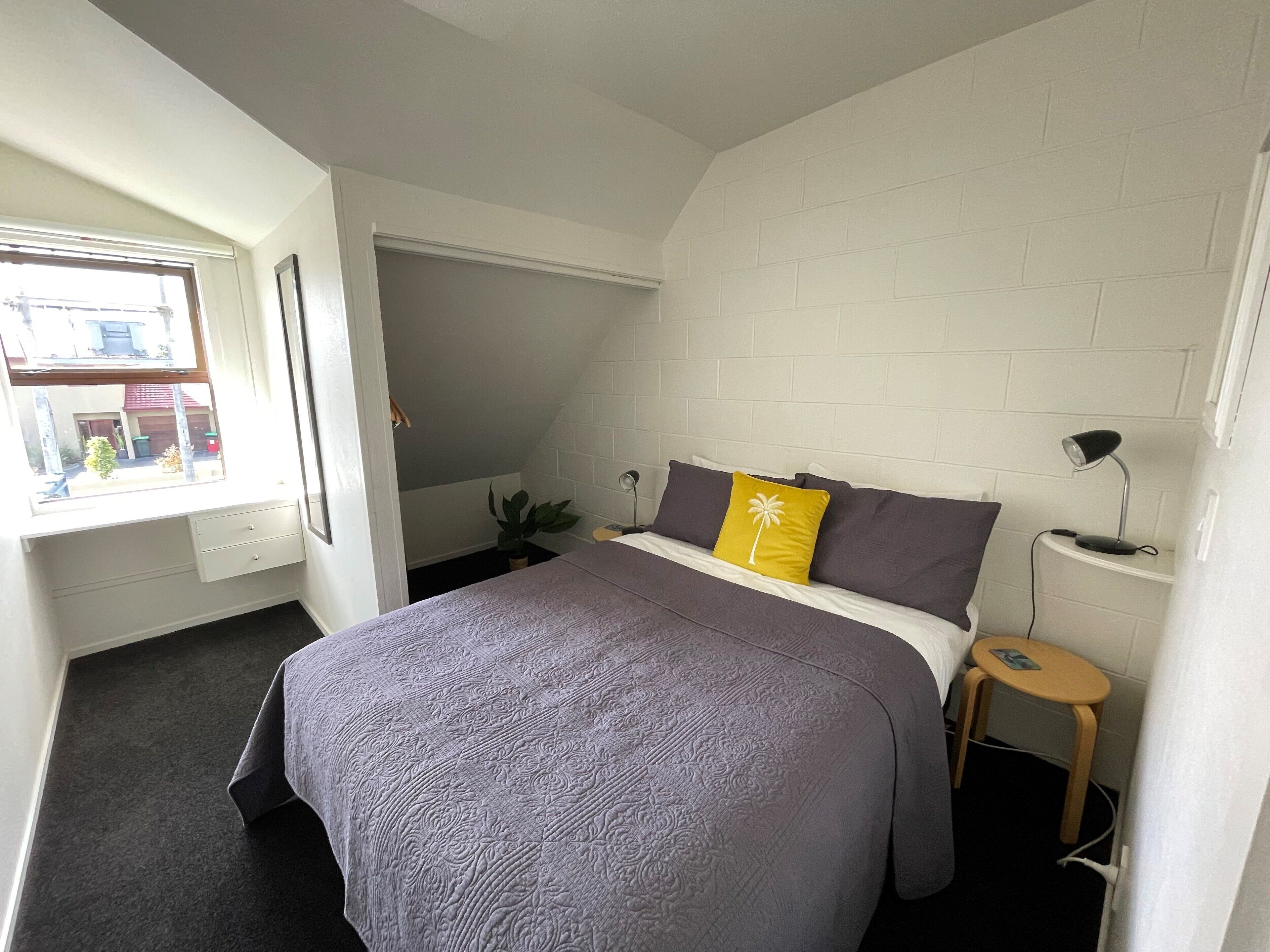 Un dormitorio con una cama, una mesita de noche, una lámpara y una ventana.