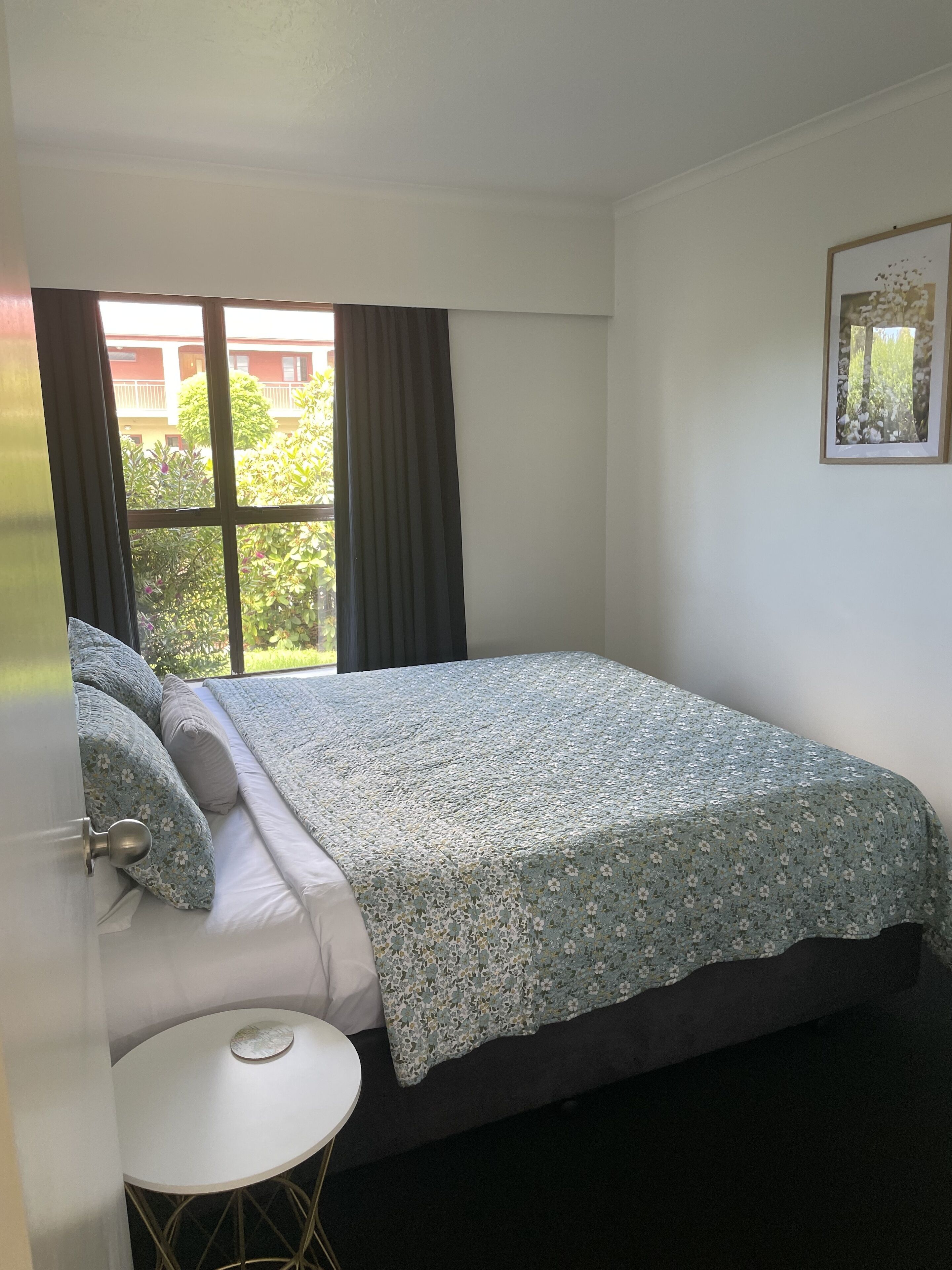 A bedroom with a bed, a small round table, and a window with curtains.