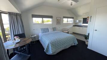 Un dormitorio con cama, escritorio, silla, ventilador de techo, ventana y kitchenette.