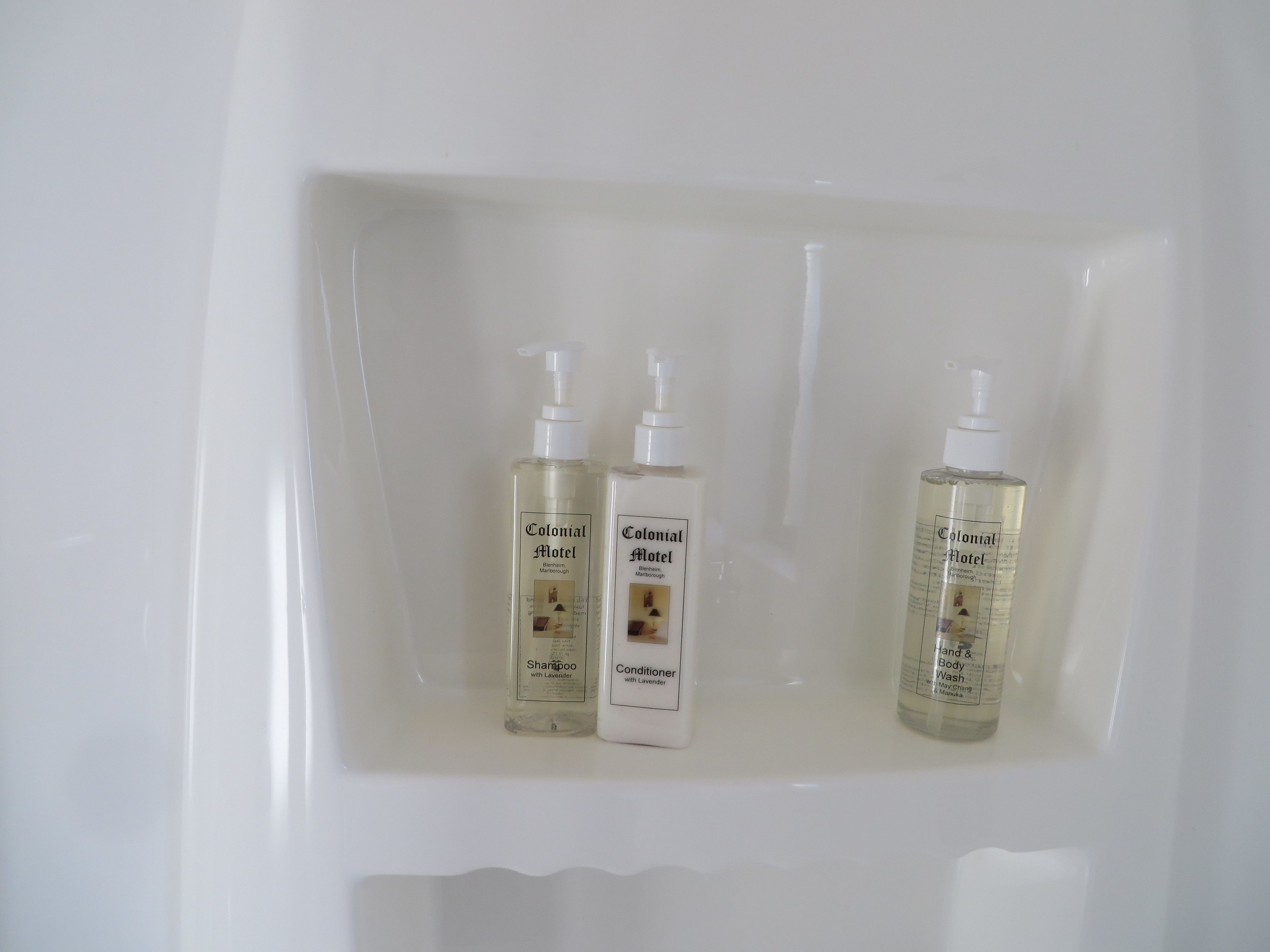 Tres botellas de productos del Colonial Motel en un estante blanco.