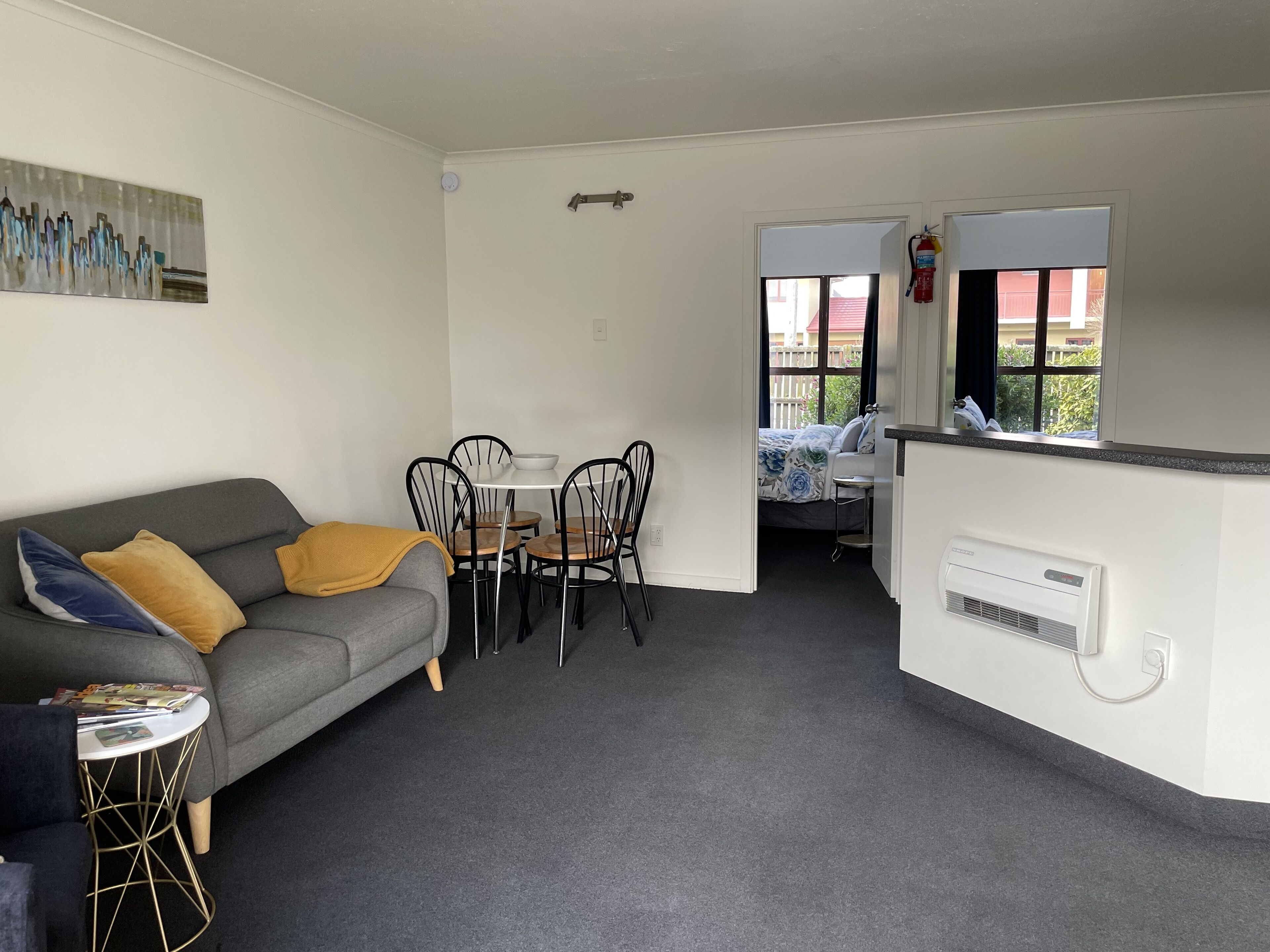 Un espacio habitable compacto con un sofá gris, una pequeña mesa redonda y una zona de kitchenette.