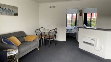Un espacio habitable compacto con un sofá gris, una pequeña mesa redonda y una zona de kitchenette.