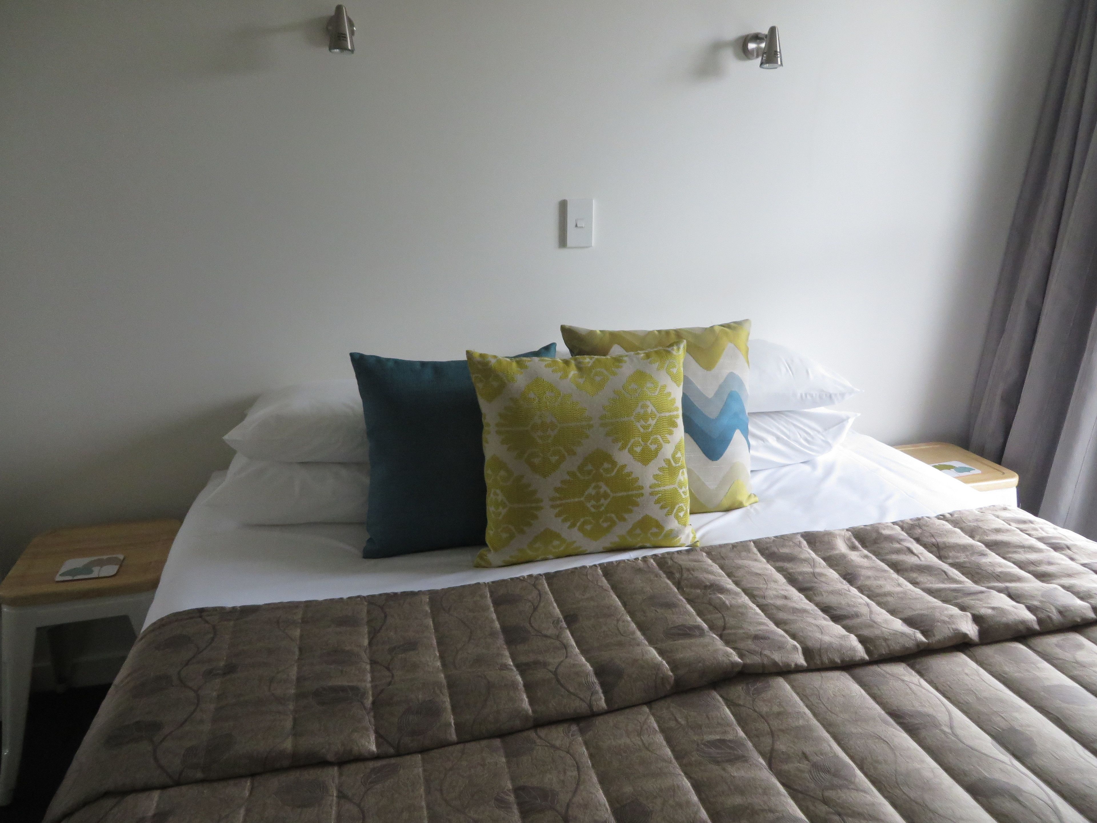 A neatly made bed with a brown quilt, two pillows, and a nightstand with a phone.