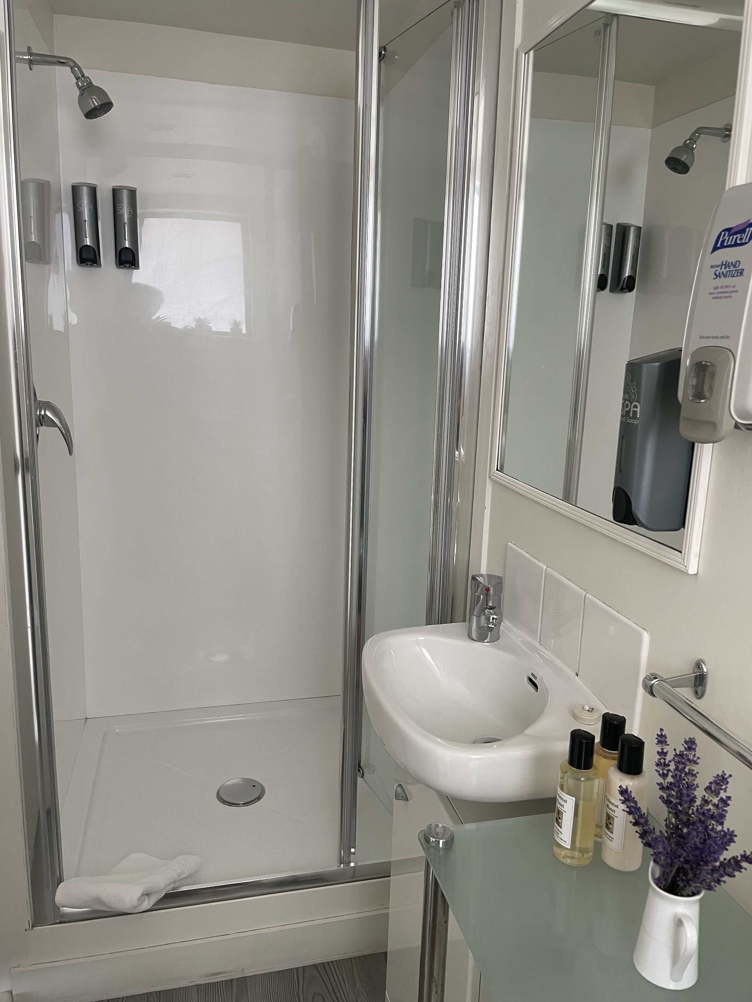 A modern bathroom with a glass-enclosed shower, a white sink, and a hand sanitizer dispenser.