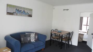 A room with a blue sofa, a dining table with four chairs, a painting on the wall, and a door leading to another room.