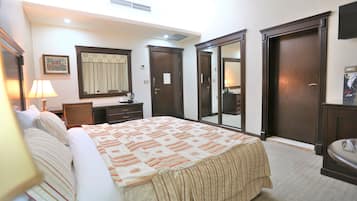 Habitación de hotel con una cama grande, una mesita de noche con lámpara, un aparador, un espejo y una puerta que da a otra habitación.