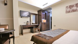 A hotel room with a bed, a desk with a chair, a TV mounted on the wall, and a wardrobe. - Hisham Hotel Amman (Amman)