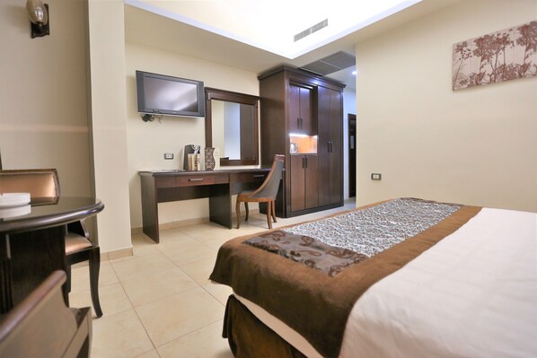 Habitación de hotel con cama, escritorio con silla, televisor montado en la pared y armario.