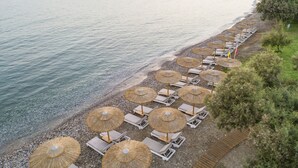 A beach with rows of sun loungers and thatched umbrellas along the shoreline.