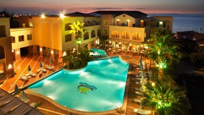 A resort pool area with a large pool, lounge chairs, and a view of the ocean at dusk.