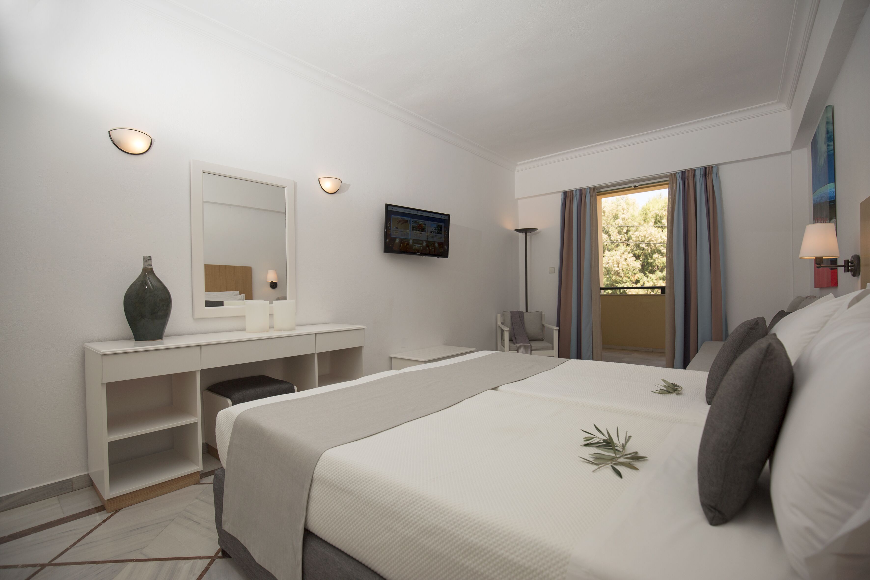 A hotel room with a bed, a desk, a chair, a mirror, a TV, and a window with curtains.