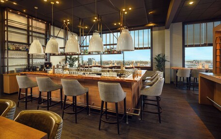 A bar area with a high bar, multiple stools, and pendant lighting.