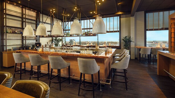 A bar area with a high bar, multiple stools, and pendant lighting. - Westcord WTC Hotel Leeuwarden (Leeuwarden)