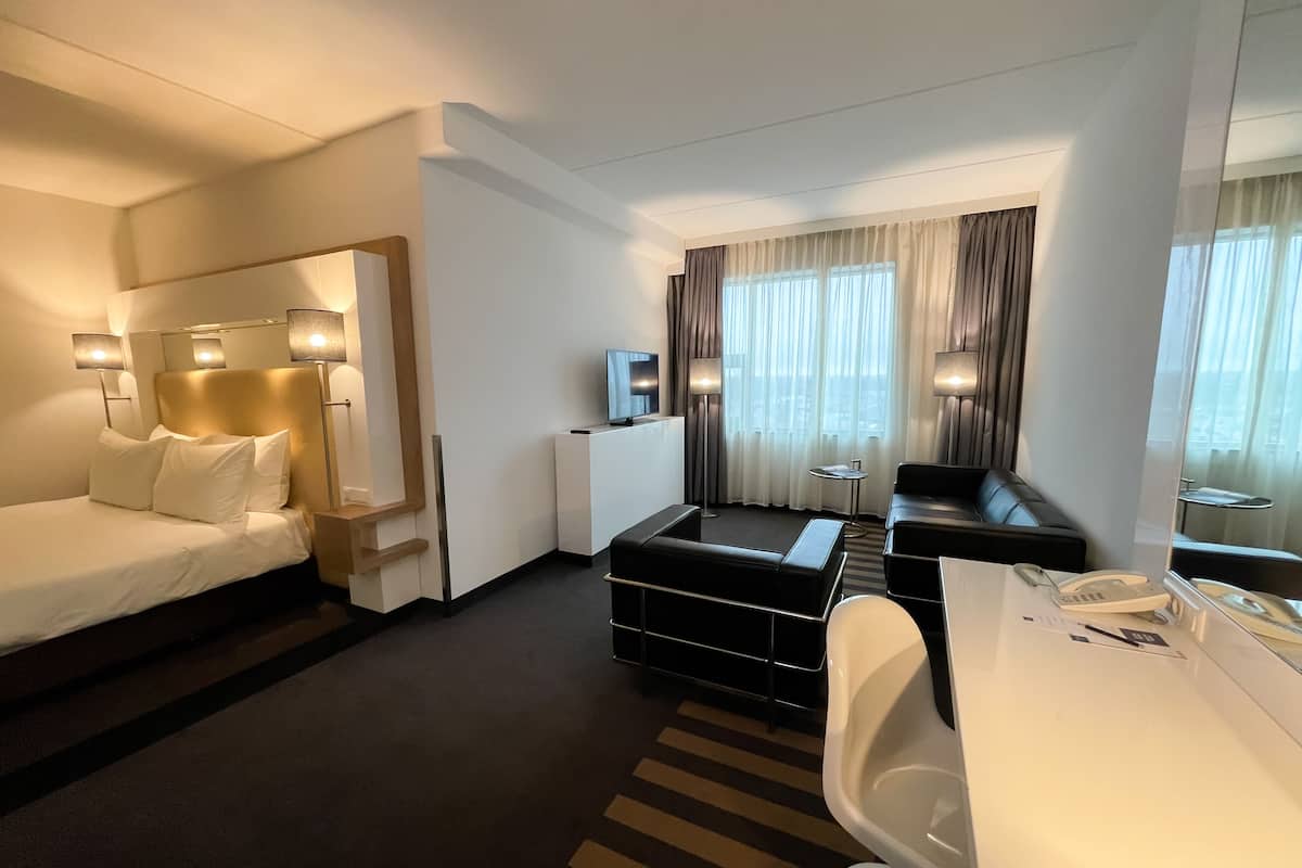 A hotel room with a bed, a desk, a chair, a sofa, and a television.