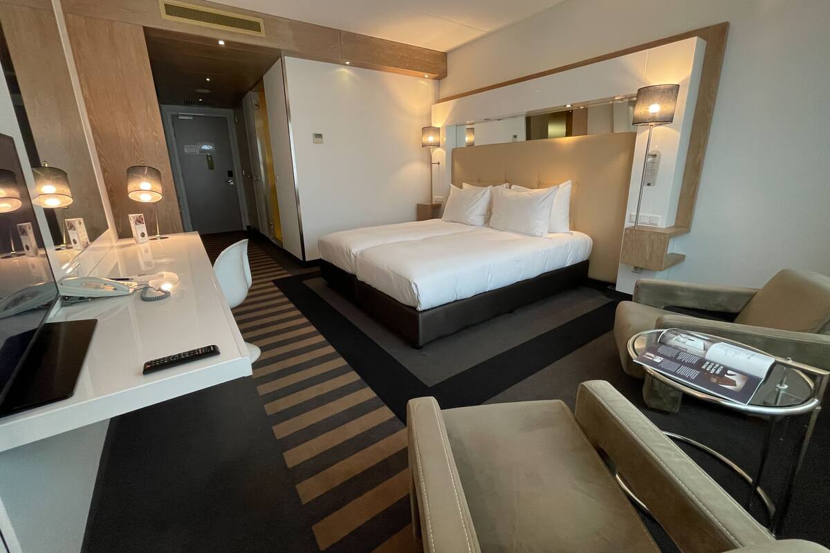 A hotel room with a bed, bedside table, chair, desk, lamp, and a mirror.