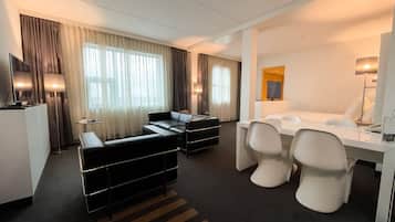 A hotel room with a sofa, a dining table with chairs, a TV, and a lamp.