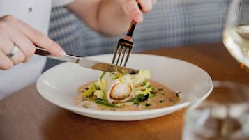 A person using a fork to eat a dish with a creamy sauce and greens.