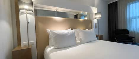 Une chambre d’hôtel avec un grand lit, deux lampes de chevet, une chaise et un miroir au mur.