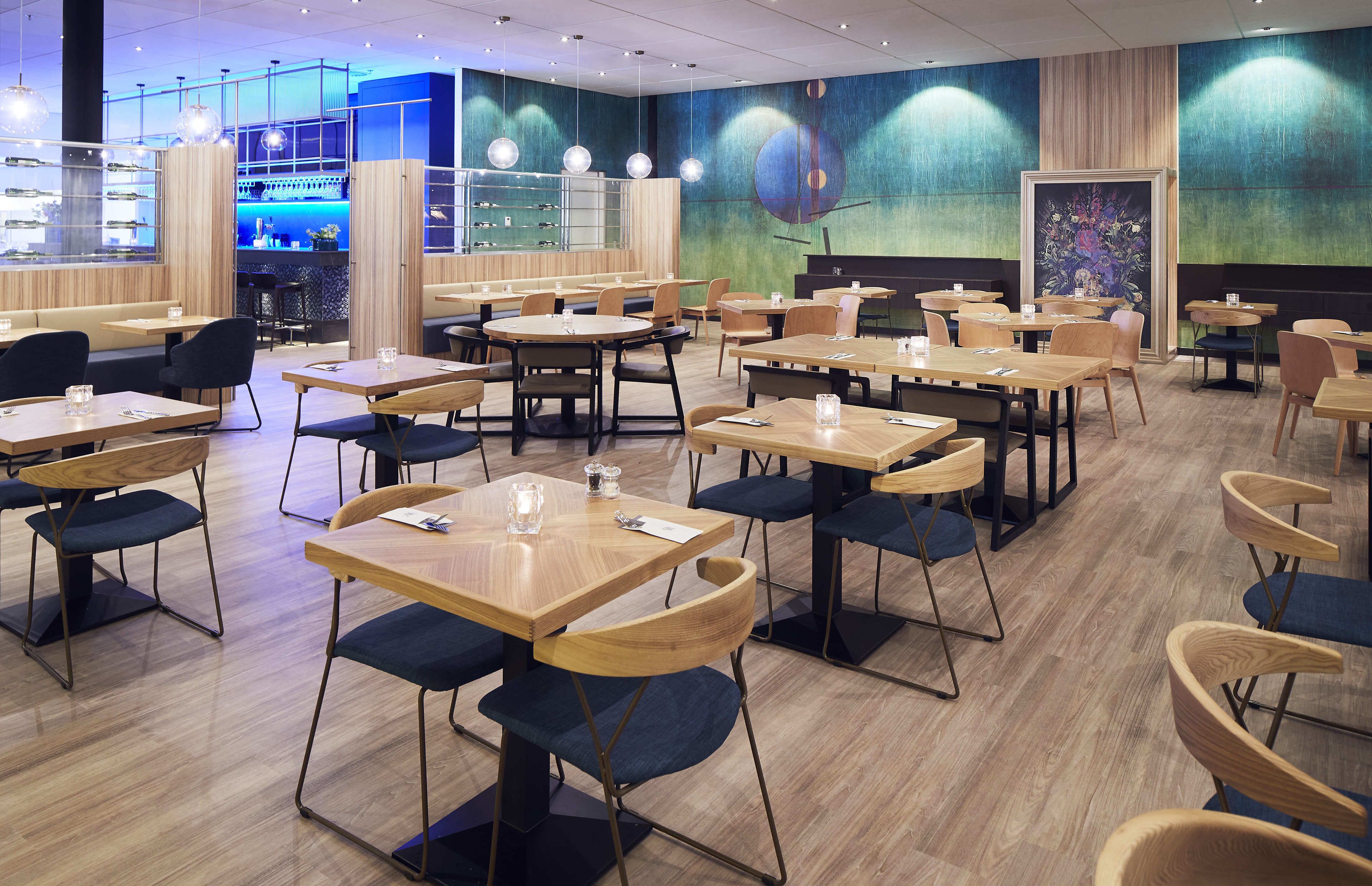 A modern restaurant with wooden tables and chairs, a bar area, and a mural on the wall.
