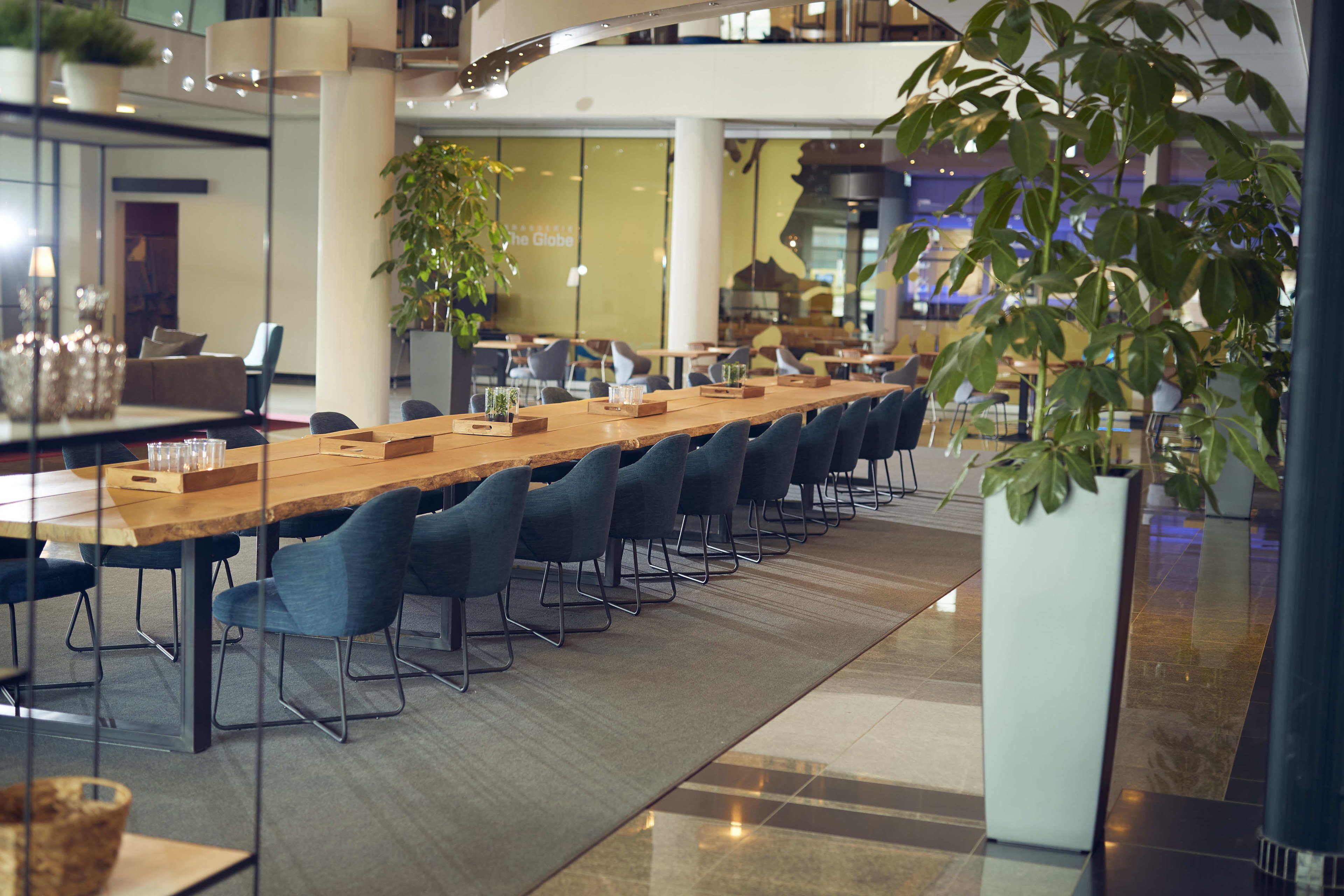 A long conference table with chairs, surrounded by glass walls and potted plants.