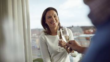 A person holding a champagne glass, standing near a window with a view of buildings.