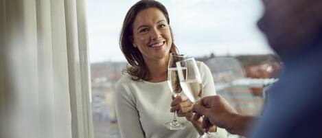 A person holding a champagne glass, standing near a window with a view of buildings.