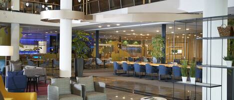 A modern hotel lobby with seating areas, a bar, and a dining space.